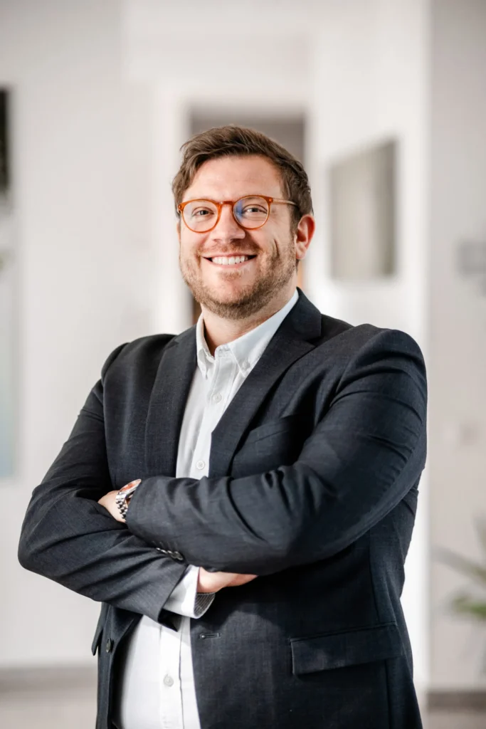 Joseph Miller, Geschäftsführer der Hecht Scheuring Finanzplanung GmbH, lächelnd mit verschränkten Armen in einem modernen Büro in Trier.